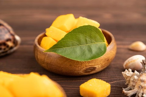 Dried and candied mango cubes in wooden bowls on brown wooden textured background. Side view, close