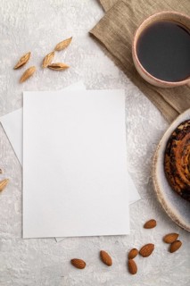 White paper invitation card, mockup with almonds, bun, cup of coffee, linen textile on gray
