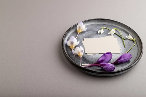 Gray paper invitation card, mockup with crocus and galanthus flowers on ceramic plate and gray