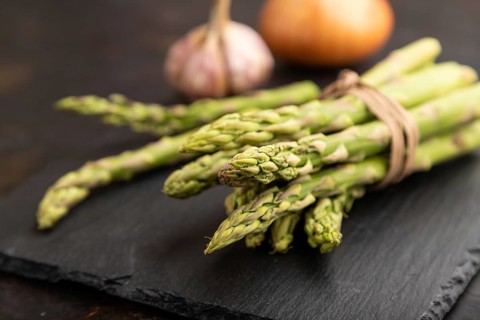 Bunch of fresh green asparagus, garlic, onion on slate board on black concrete background. Side