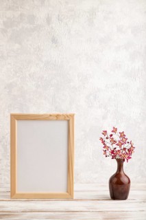 Wooden frame with purple barrenwort flowers in ceramic vase on gray concrete background. side view,