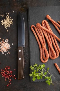 Traditional polish smoked pork sausage kabanos on a slate cutting board with salt and pepper on