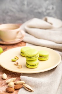 Green macarons or macaroons cakes with cup of coffee on a brown concrete background and linen