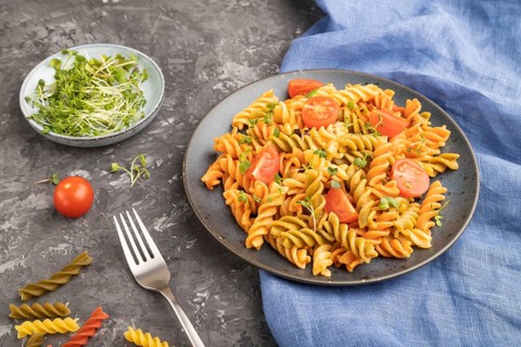 Tortiglioni semolina pasta with tomato and microgreen sprouts on a black concrete background and