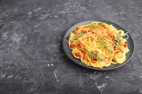 Corn noodles with tomato sauce and arugula on a black concrete background. Side view, close up,