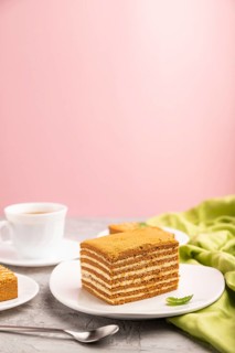 Homemade honey cake with milk cream and mint with cup of coffee on a and pink background and green