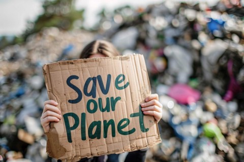 Activist with cardboard sign with text 'Save our planet' in front of blurry mountain of garbage. KI
