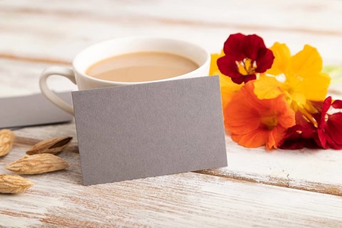 Gray paper business card mockup with orange nasturtium flower and cup of coffee on white wooden