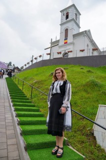 Young woman in folk traditional costume in front of a church on a green hill, woman in traditional