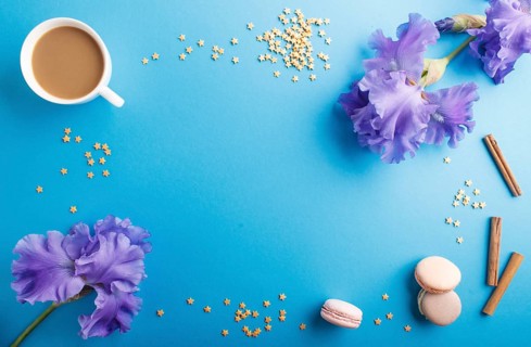 Purple iris flowers and a cup of coffee on a blue pastel background. Morninig, spring, fashion
