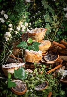 Fresh biscuits sprinkled with icing sugar, surrounded by green leaves and flowers, dried orange