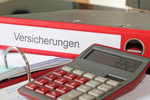 Symbolic image: Folder with insurance policies and calculator on a desk