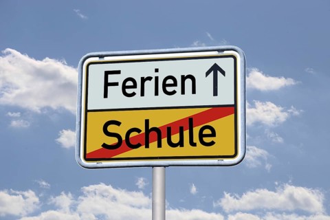 Symbolic image: German town exit sign with the words Schule/Ferien against a blue sky