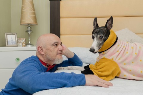 A mature man gazes lovingly at his pet, a Greyhound wearing an orange coat to keep warm, during a