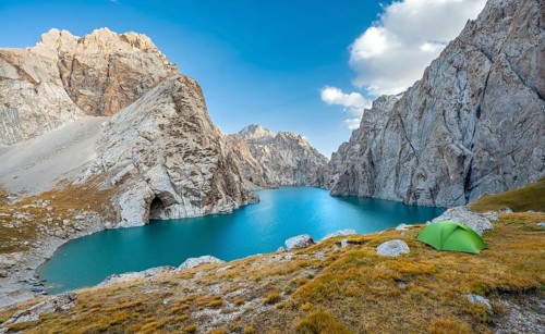 Green tent at the turquoise mountain lake Kol Suu with rocky steep mountains, Kol Suu Lake, Sary