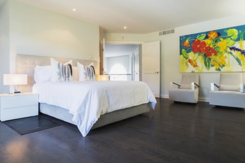 Master bedroom with queen size bed, white lacquered nightstands, upholstered armchairs and dark