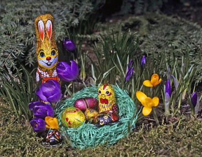 A colourful Easter bunny stands next to a nest of Easter eggs surrounded by purple and yellow