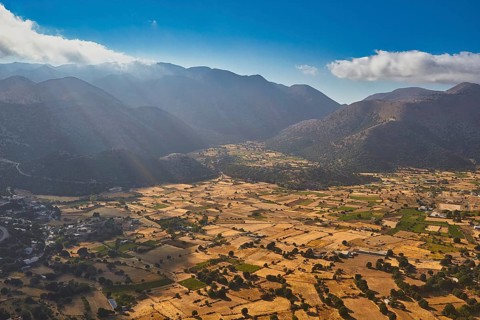 Aerial view of a valley with fields, crossed by sunbeams and surrounded by mountains, Askifou