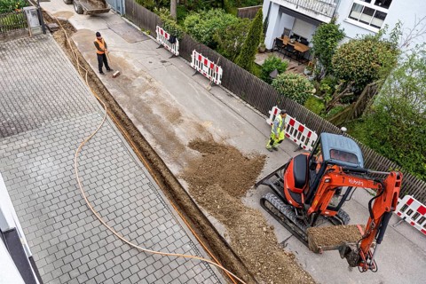 Construction workers lay fibre optic cable in trench under asphalt, cable trench, excavator,
