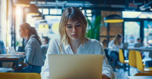 A business woman is sitting at a table with a laptop in front of her working remotely with the team