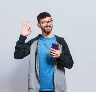 Pleasant person holding cellphone and winking, smiling boy with cellphone making ok sign, concept