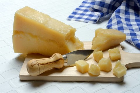 A piece of Parmesan cheese and chopped pieces of cheese on a wooden board