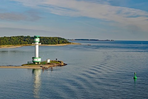 White-green lighthouse on a coast with wide water surfaces and a green buoy in the foreground,