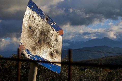 A rusty, tattered road sign in front of a mountainous landscape under a cloudy sky, Lefka Ori,