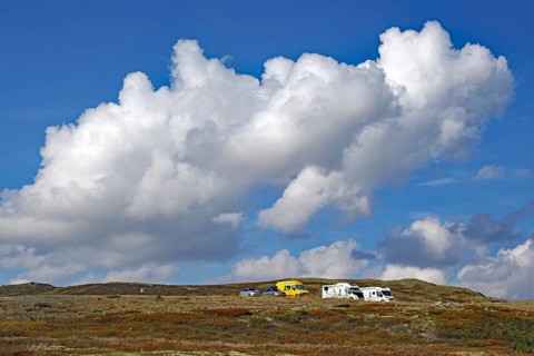 Motorhomes on a hilly landscape under large, dramatic cloud formations in the blue sky, autumn,