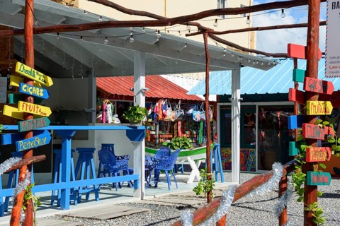 A Caribbean market with colourful signs and souvenirs under an outdoor wooden structure, Bayahibe,