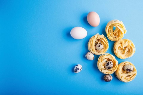 Raw uncooked tagliatelle pasta with quail eggs on a blue pastel background. top view. copy space.