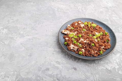 Quinoa porridge with green pea and chicken on ceramic plate on a gray concrete background. Side