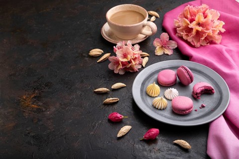 Purple macarons or macaroons cakes with cup of coffee on a black concrete background and pink