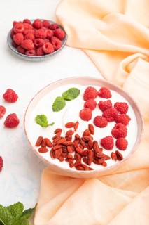 Yogurt with raspberry and goji berries in ceramic bowl on white concrete background and orange
