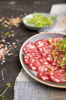 Slices of smoked cervelat salami sausage with spinach microgreen, salt and pepper on black concrete