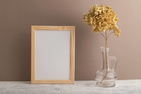 White wooden frame mockup with dried hydrangea in glass on beige paper background. Blank, vertical