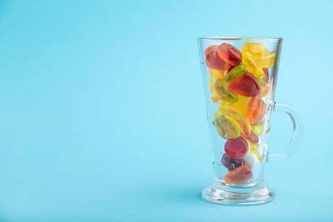 Various fruit jelly candies in drinking glass on blue pastel background. side view, copy space