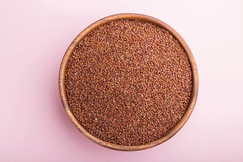 Wooden bowl with raw red quinoa seeds on a pastel pink background. Top view, flat lay, close up