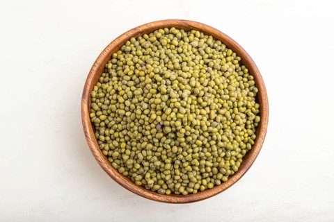 Wooden bowl with raw green mung bean on a white wooden background. Top view, flat lay, close up