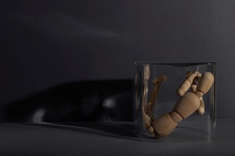 Wooden mannequin locked in a glass cube on gray background. captivity, break rules, loneliness,