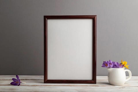 Brown wooden frame mockup with snowdrop crocus flowers on gray paper background. Blank, vertical