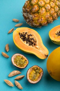 Ripe cut papaya, pineapple, melon, passion fruit, almonds on blue pastel background. Side view,