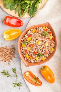 Buckwheat porridge with vegetables in clay bowl on a gray concrete background and linen textile.
