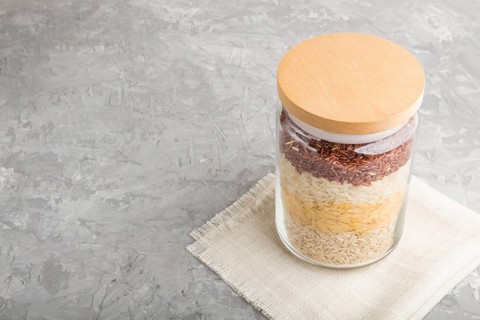 Glass jar with different kinds of rice poured in layers on a gray concrete background. side view,