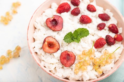 Rice flakes porridge with milk and strawberry in ceramic bowl on white concrete background and blue