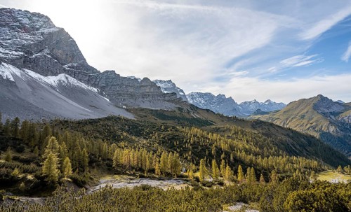 Mountain panorama with steep rocky peaks, yellow-coloured larches in autumn, hike to the summit of