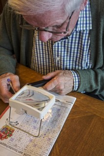 Elderly man suffering from presbyopia, myopia, short-sightedness looking at crossword puzzle though