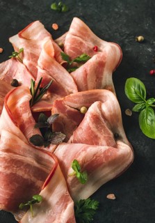 Raw bacon, sliced, with micro greenery and spices, on a black background, close-up