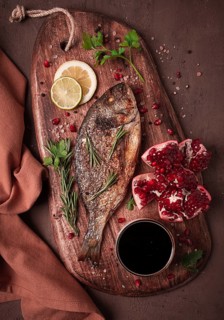 Fried dorado fish, with spices and herbs, on a wooden board, pomegranate sauce, close-up, no people