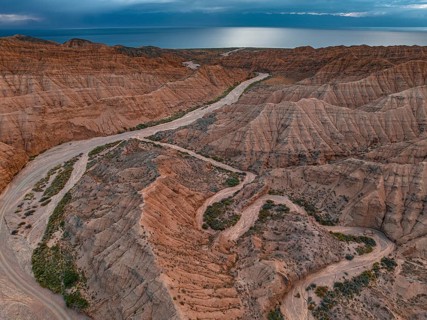 River bed runs through a landscape of eroded hills, badlands, Issyk Kul Lake in the background,
